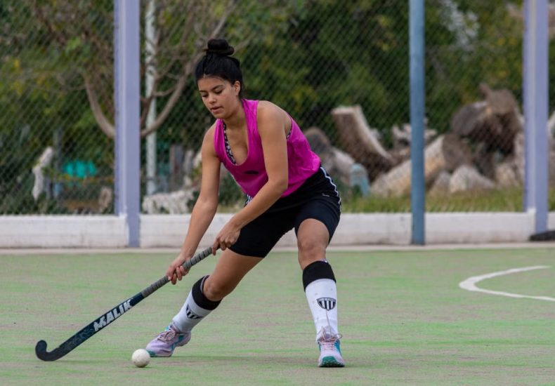 A young female athlete playing field hockey outdoors on a sunny day.