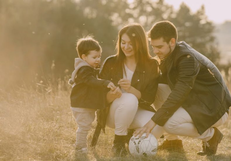 A cheerful family bonding outdoors with a soccer ball, enjoying a sunny day in the grass.
